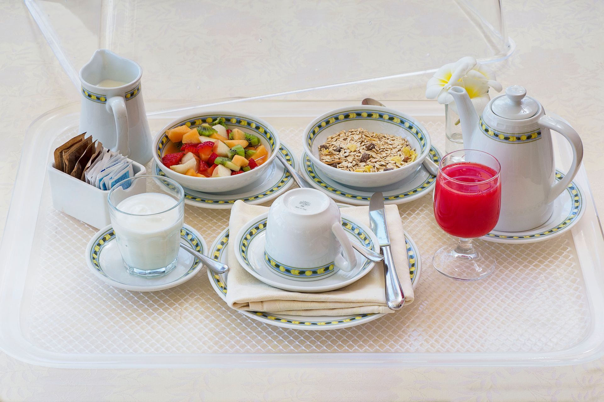 Tea set with sandwiches, fruit salad, pastries, milk, and red juice on a white tray