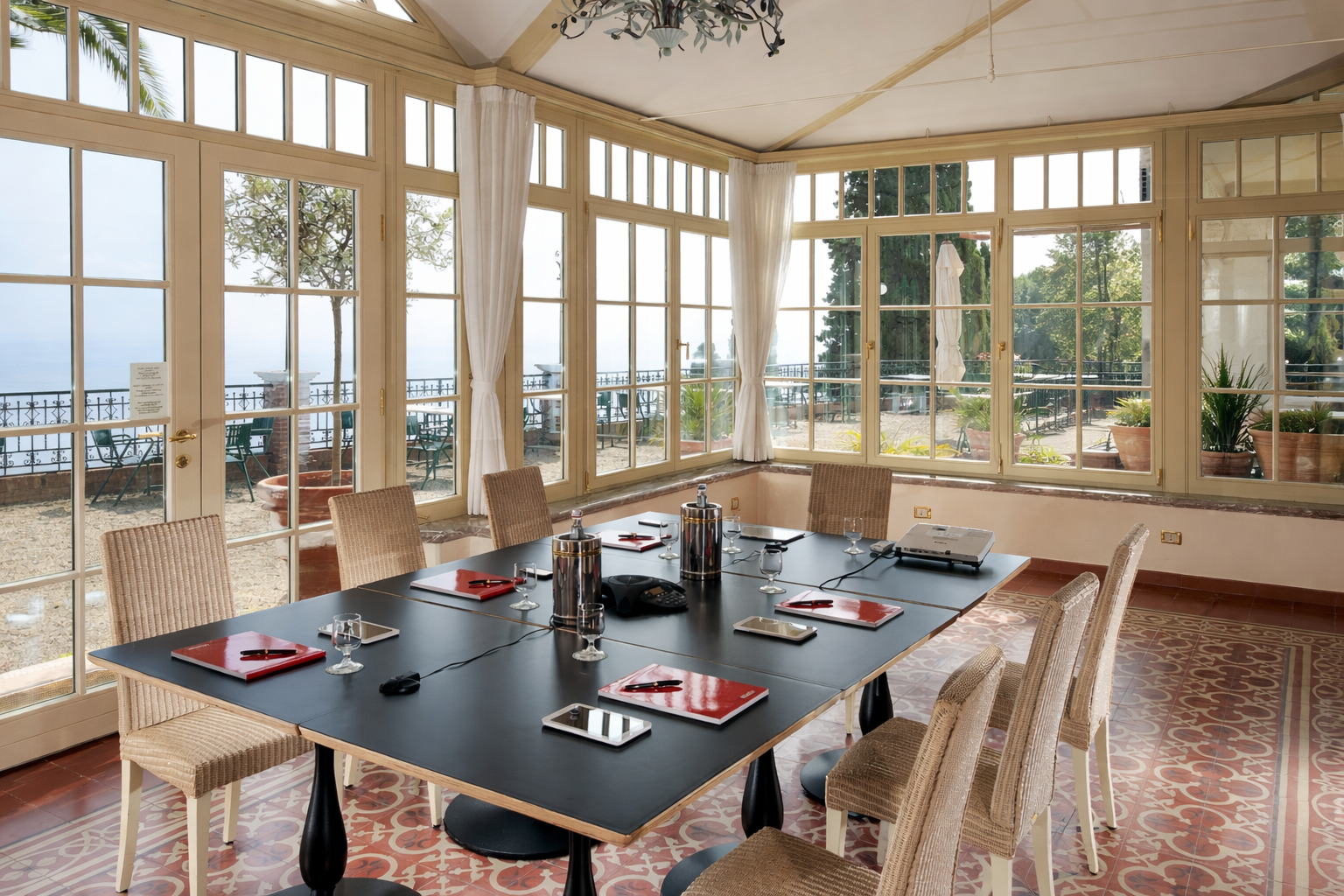 Elegant dining room with a set table, wicker chairs, and large windows overlooking a waterfront.