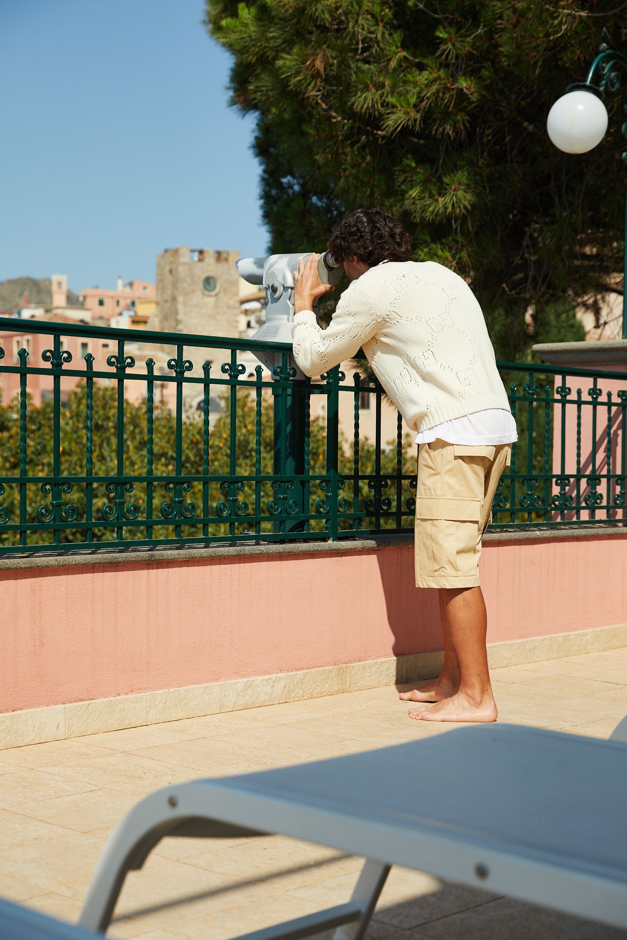 Person leaning on a balcony railing, looking out over a sunny cityscape.