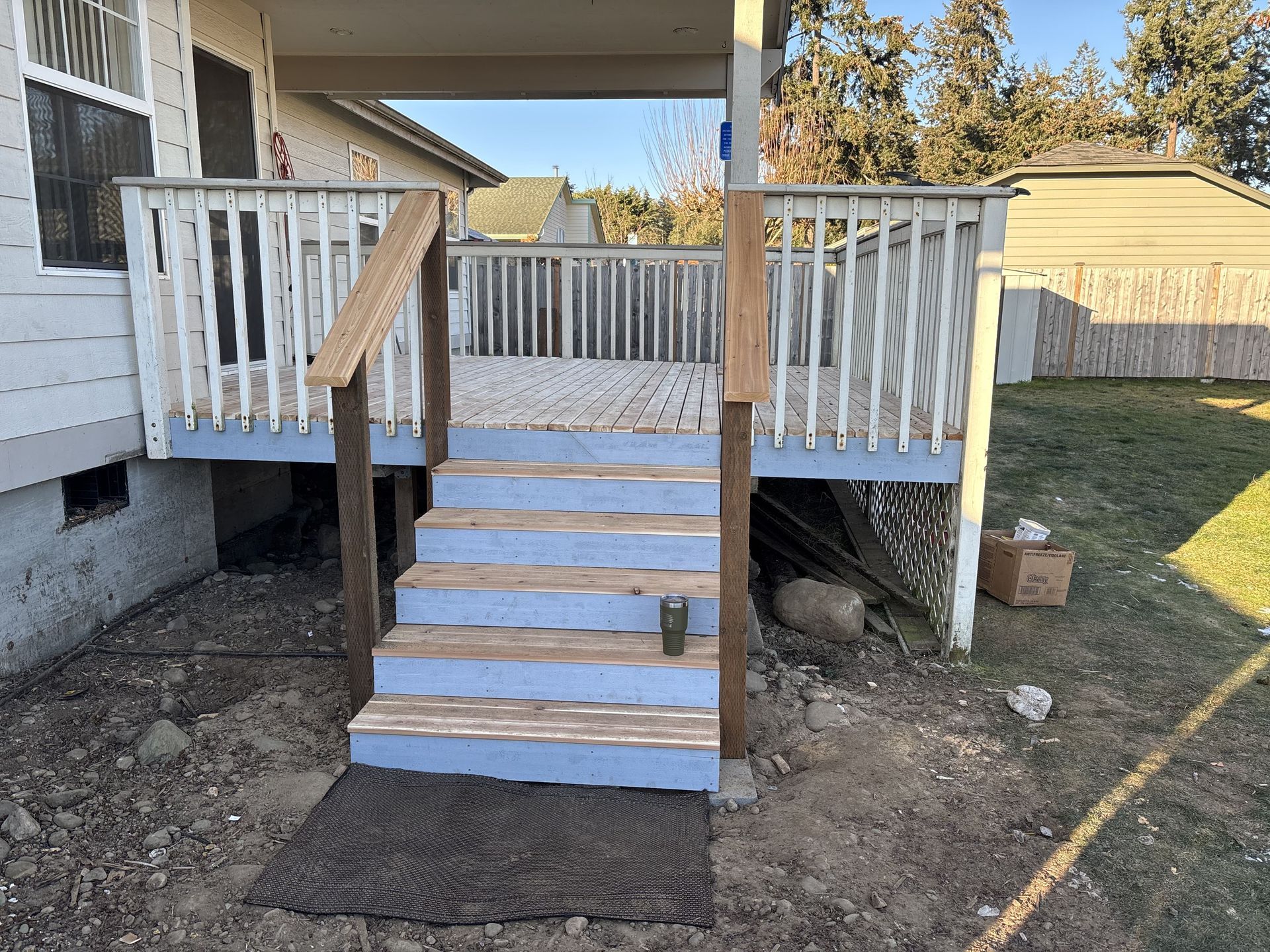 A wooden deck with stairs leading up to it is in the backyard of a house.