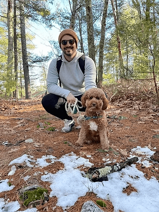 Man with small brown dog on a forest trail, some snow on the ground.