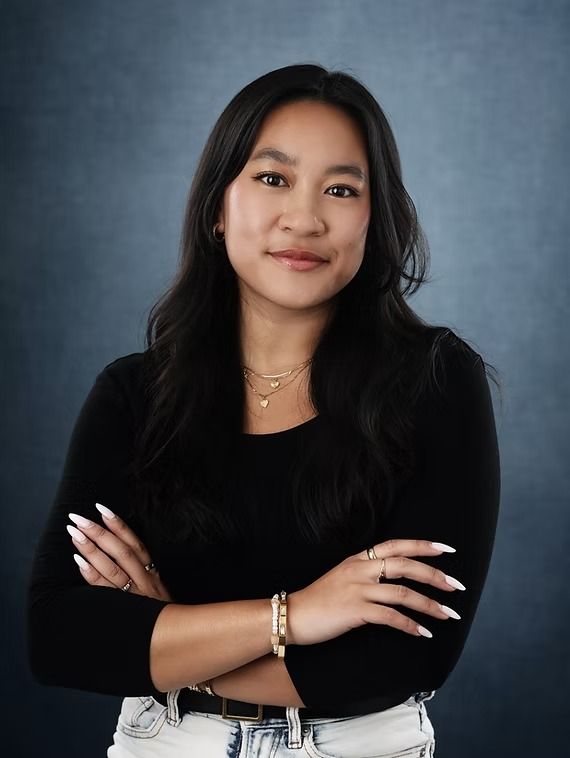 Woman with dark hair and a black top, arms crossed, smiling.