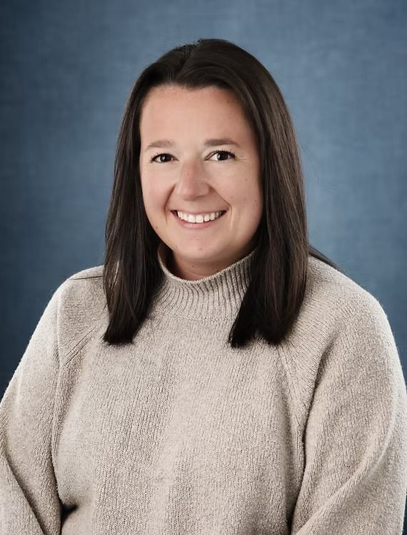 Woman with shoulder-length dark hair, smiling, wearing a light-colored sweater, against a blue background.