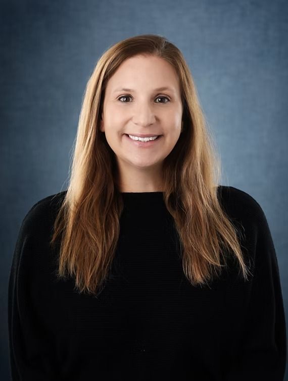 Woman with long blonde hair smiles, wearing a black sweater, against a blue background.