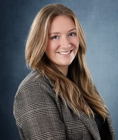 Woman with blonde hair wearing a plaid blazer, smiling, against a blue backdrop.