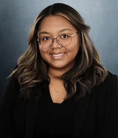 Woman with glasses, smiling, wearing a black blazer, against a blue and gray background.