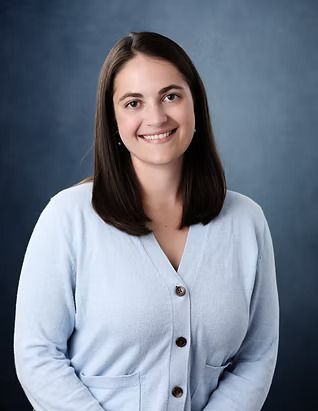 Woman with dark hair, smiling, wearing a light blue cardigan, against a blue background.