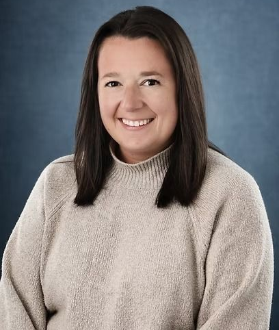 Woman with dark hair smiles, wearing a light-colored sweater against a blue background.