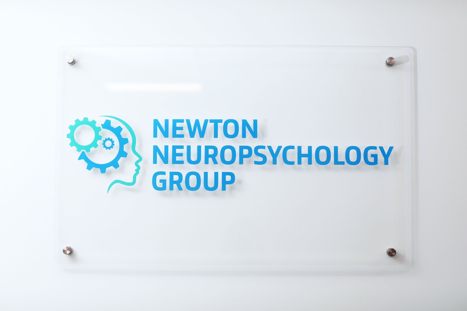 Clear wall sign for Newton Neuropsychology Group, logo of gear/head in teal, blue text on white wall.