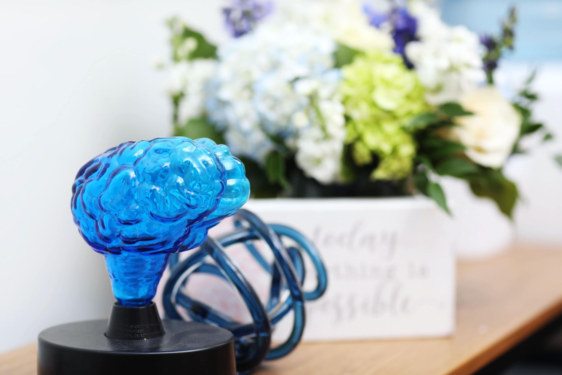 Blue brain-shaped glass sculpture on a base, with a bouquet of flowers in the background.