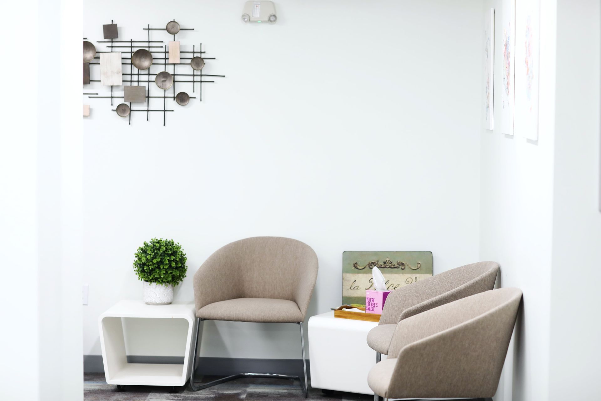 Waiting room with beige chairs, white tables, and wall art.