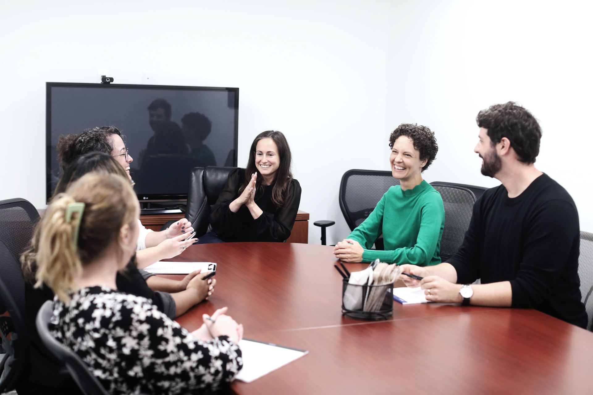 People seated around a conference table in a meeting, smiling and talking.
