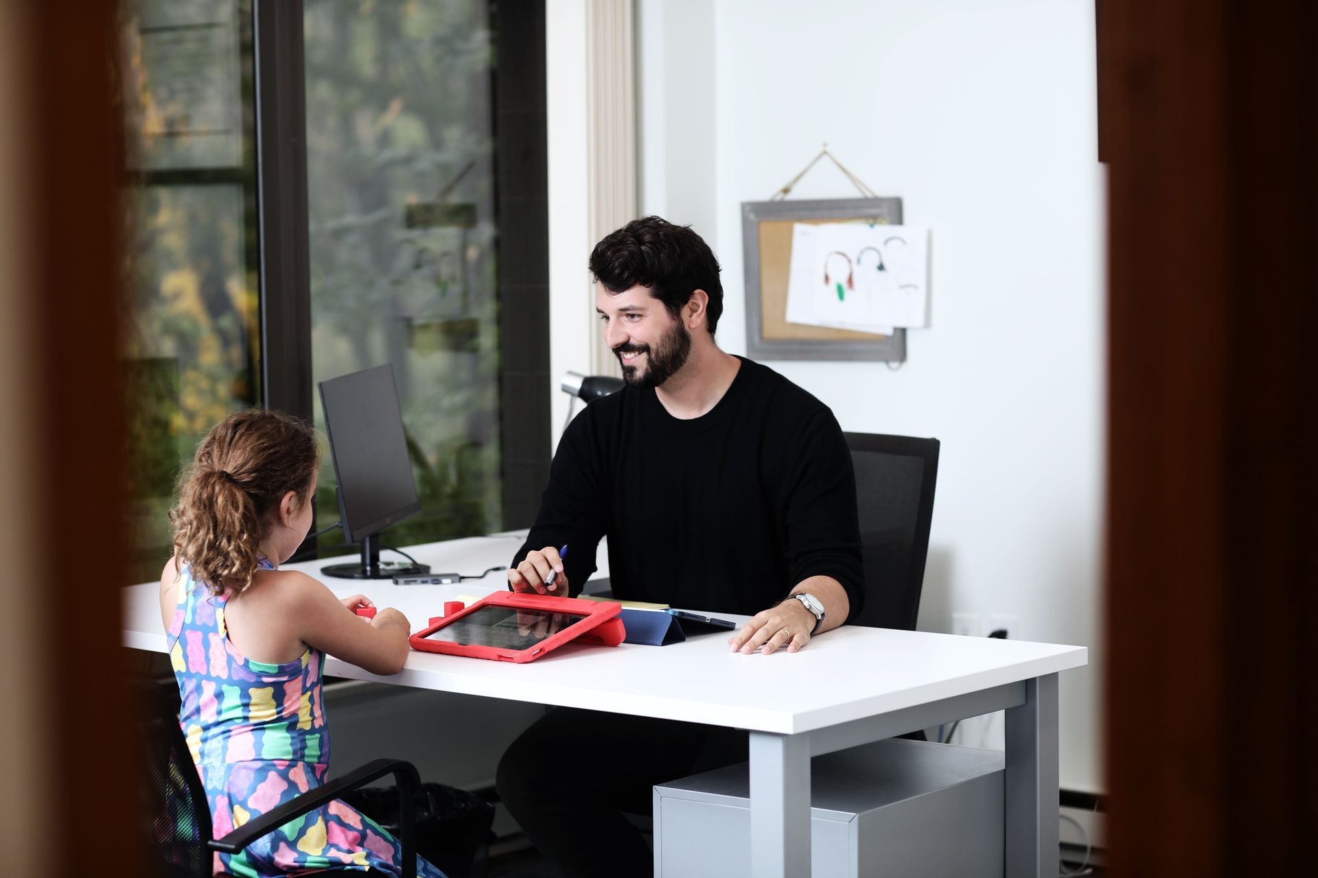 Man sitting at a desk smiles at a child. The child sits opposite him. They are in an office setting.