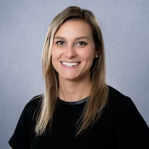 Woman with blonde hair, smiling at the camera, wearing a black top against a gray backdrop.
