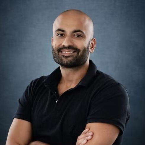 Bald man with a trimmed beard and a black polo shirt, arms crossed, smiling.