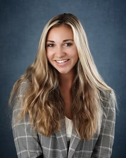 Woman with brown hair and arms crossed, wearing a black top against a blue backdrop.