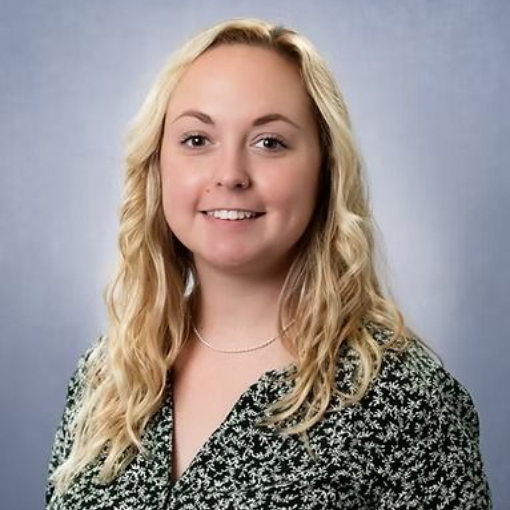 Woman with blonde wavy hair smiles at the camera, wearing a patterned top, against a blue background.