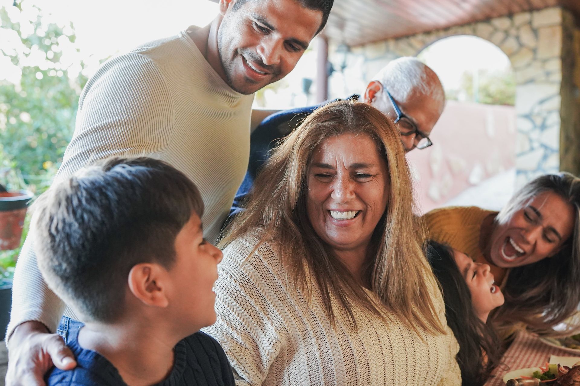 Family laughing together outdoors. People gathered around a table; a child smiles at an older woman.