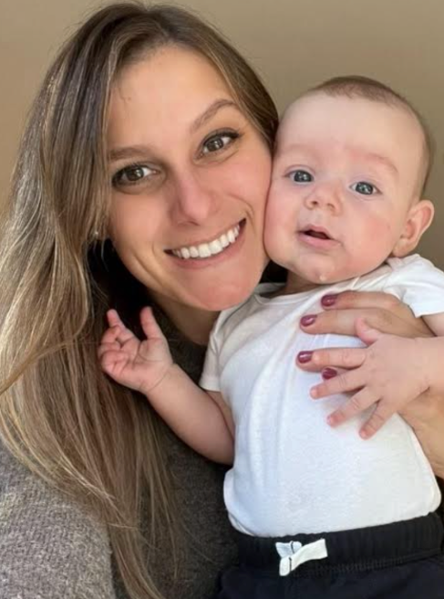 Man with dark hair and stubble in a denim shirt, looking directly at the camera against a blue backdrop.