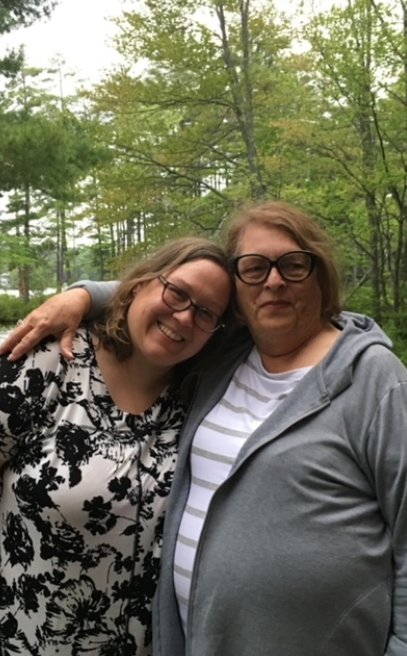 Woman with dark hair, smiling, wearing a light blue cardigan, against a blue background.