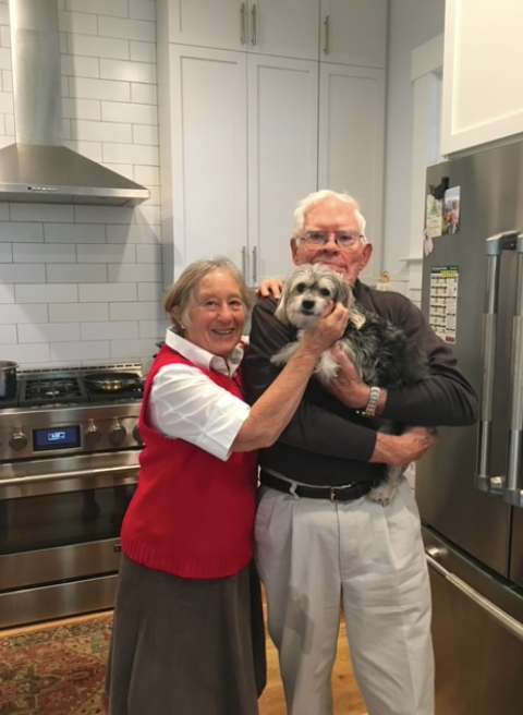 Woman smiling, wearing a white and red floral top, with shoulder-length brown hair, against a blue background.