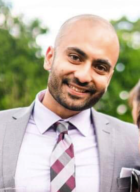 Woman with glasses smiles, arms crossed, wearing a black top against a blue background.