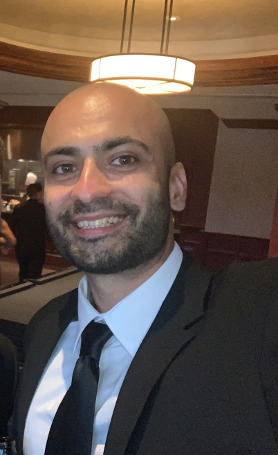Woman smiling, wearing a white and red floral top, with shoulder-length brown hair, against a blue background.