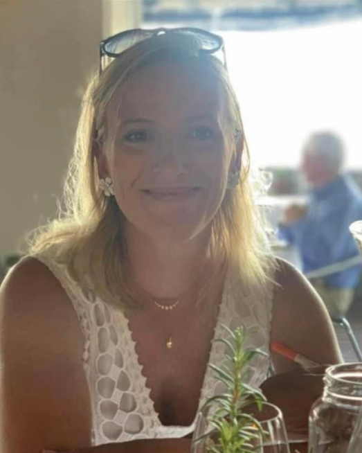 Woman with dark hair, smiling, wearing a light blue cardigan, against a blue background.
