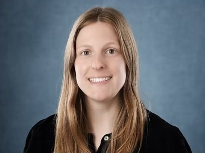 Woman with long blonde hair, smiling, in front of a blue background.