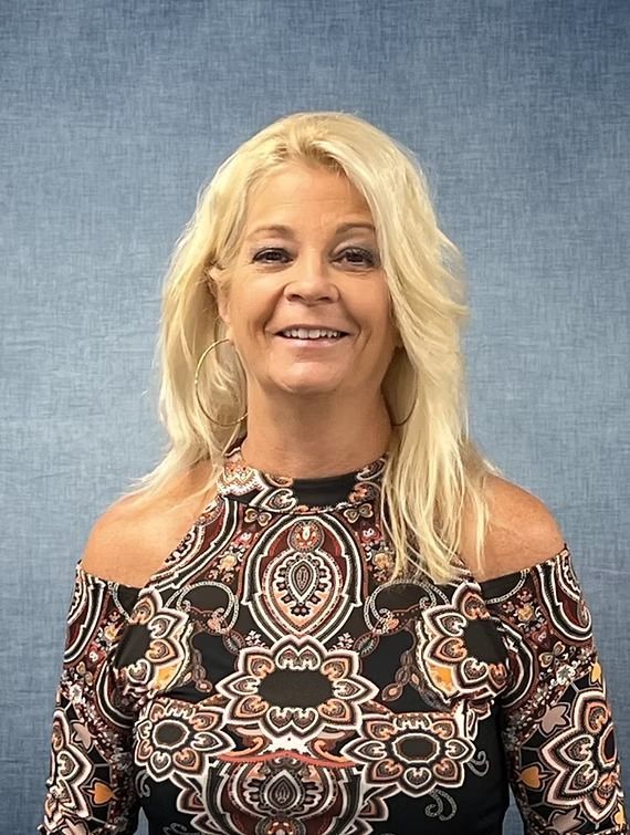 Blonde woman in patterned top smiles at camera; blue background.