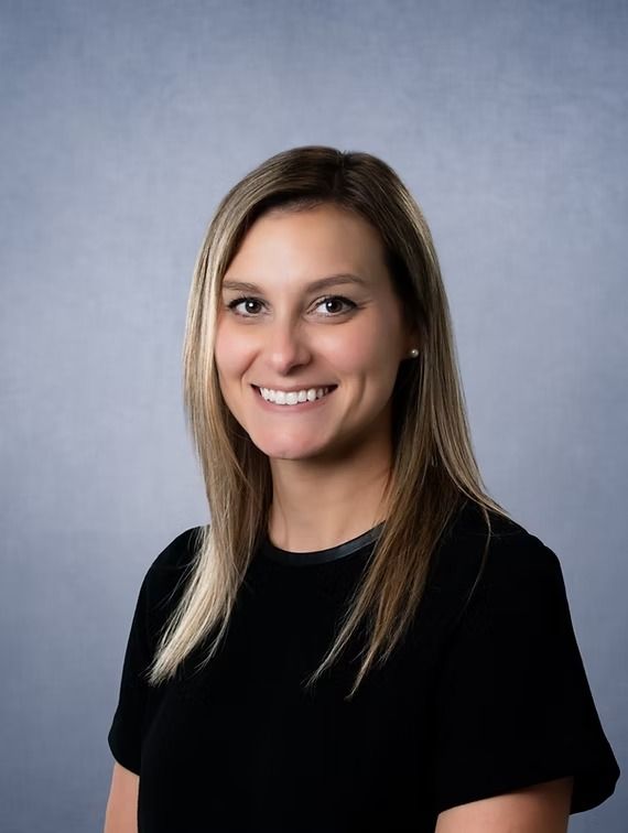 Woman with blonde hair smiling, wearing a black top against a gray backdrop.
