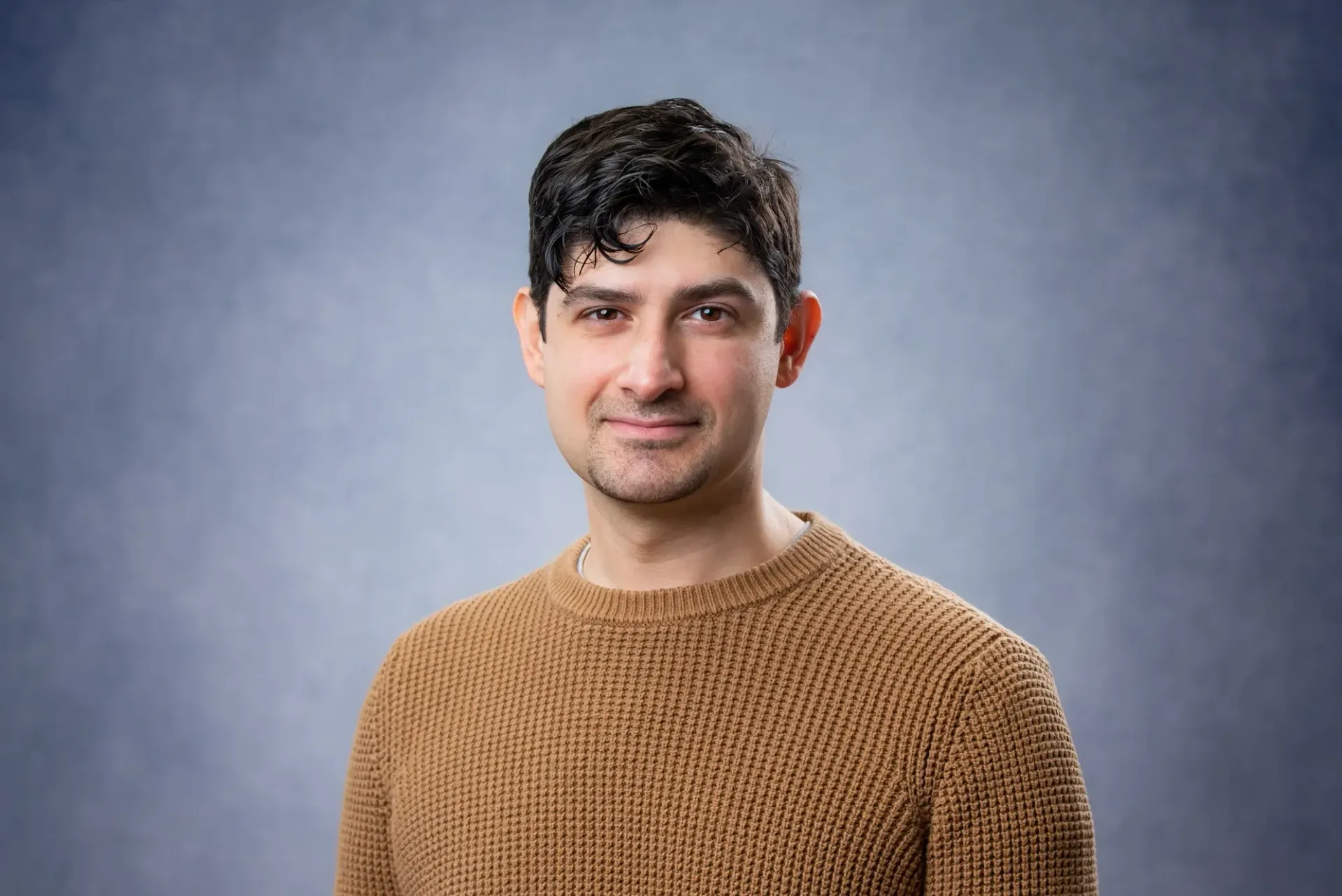 Woman with glasses smiles, arms crossed, wearing a black top against a blue background.