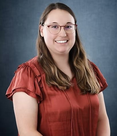 Woman wearing glasses and a red blouse smiles at the camera against a blue background.