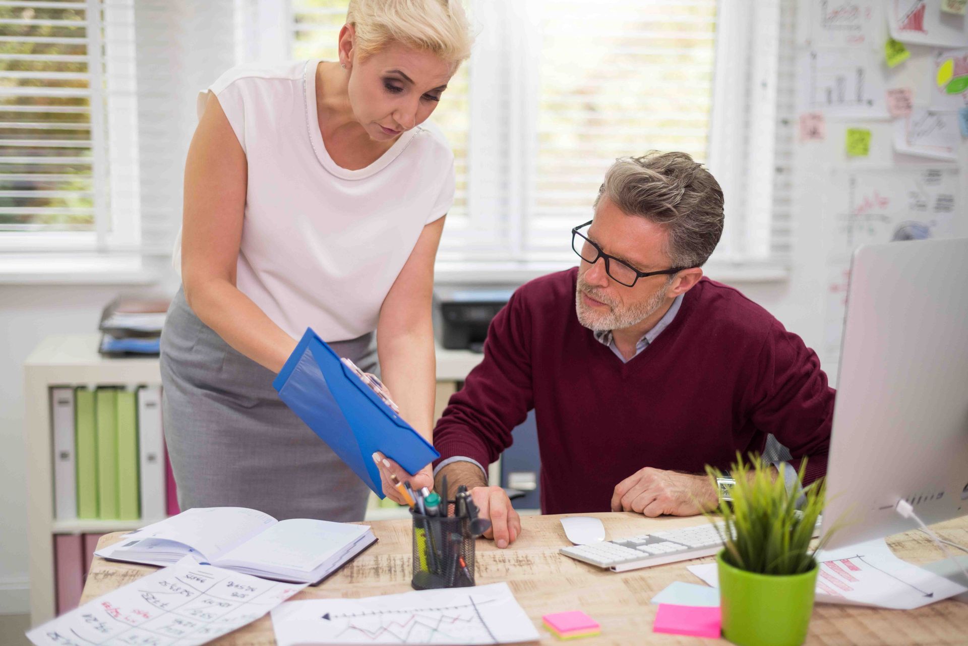 Woman showing paperwork to a man at a desk in an office.