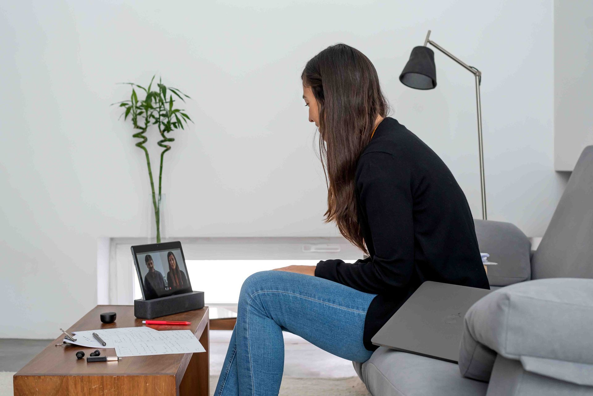 Woman on couch having a video call on a tablet, writing notes on a table.