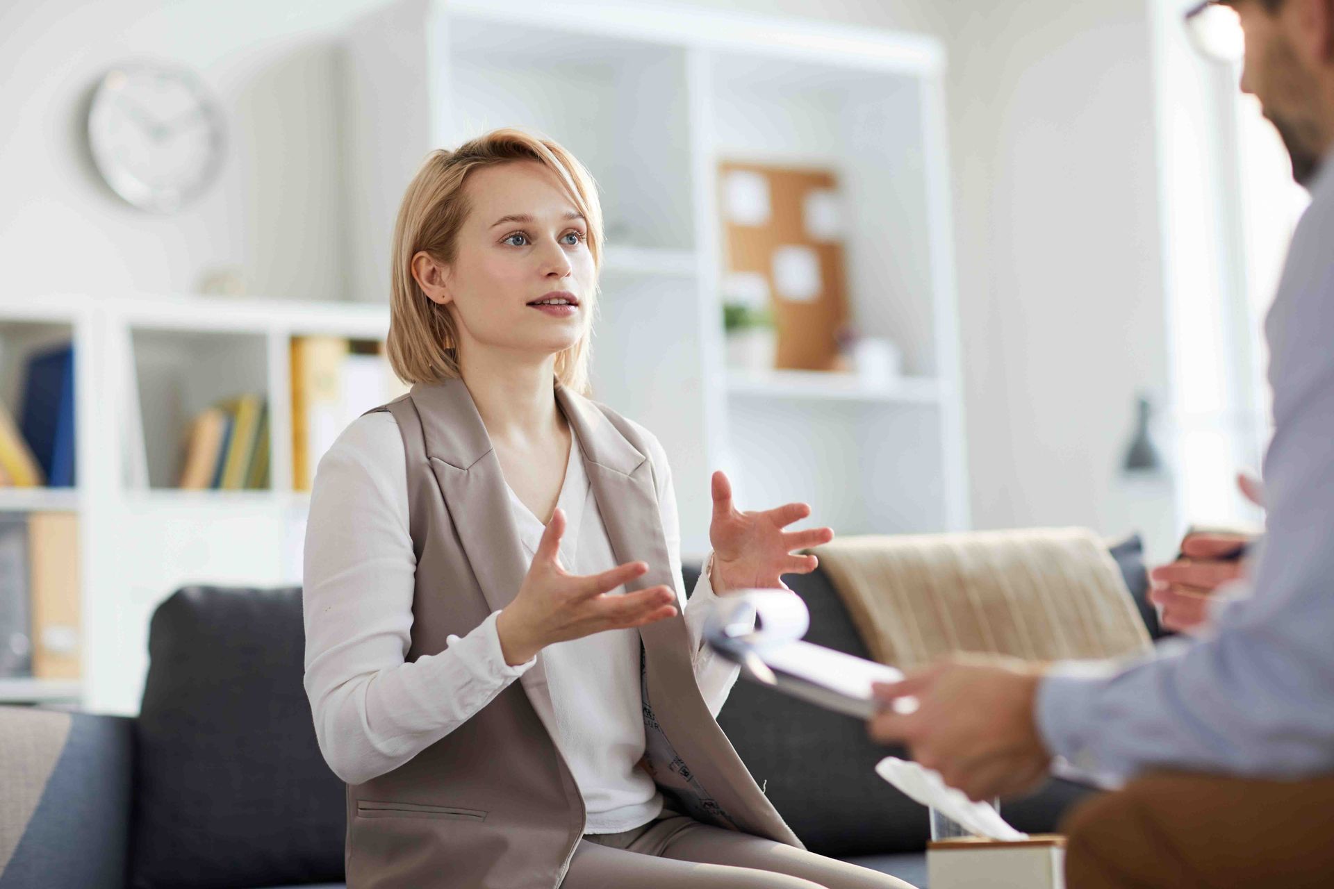 Woman in vest gesturing, speaking to person seated; counseling setting, tissue box nearby.