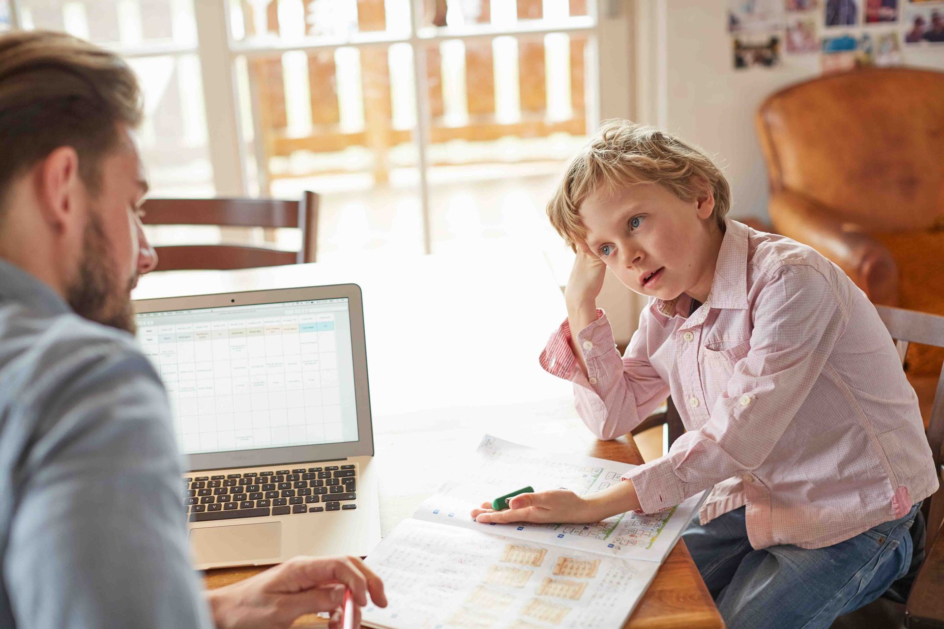 Man using laptop at table with a boy looking at a map, pondering.