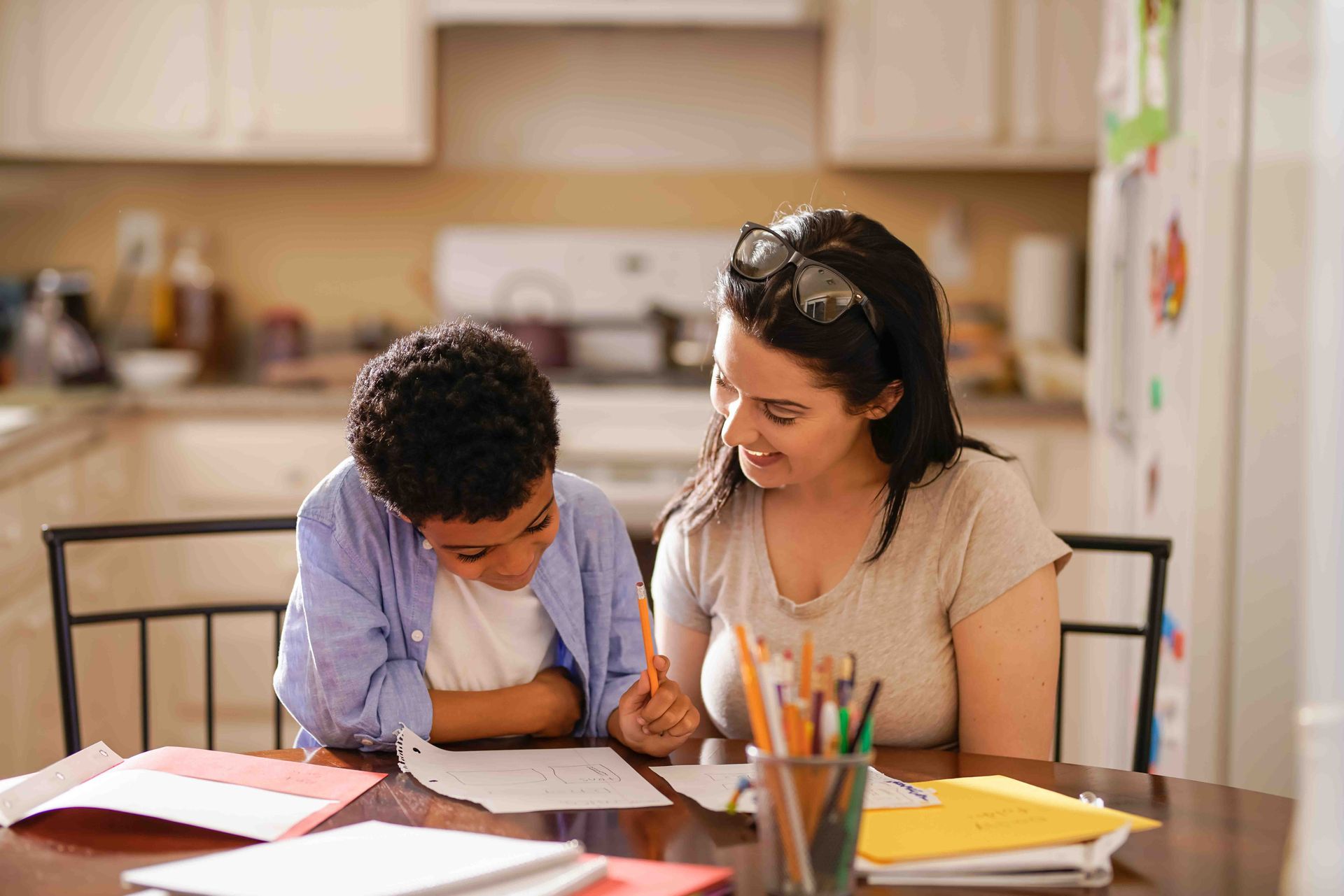 A person helps a child with homework at a kitchen table.