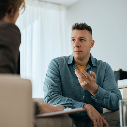 Man talking, gesturing to a person out of frame; indoors, possibly a therapy session.