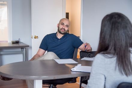 Man and person facing each other at a round table, discussing with documents. Neutral office setting.