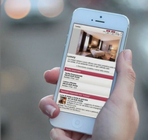 Persona con uno smartphone in mano, che consulta i dettagli di un hotel di lusso. Sfondo sfocato.
