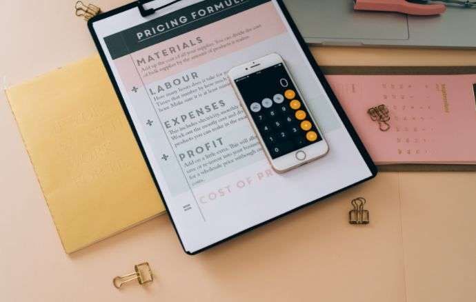 Blocco appunti con formula di determinazione dei prezzi, telefono con app calcolatrice.