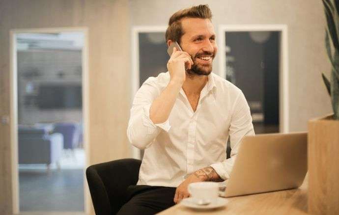 Un uomo in camicia bianca sorride durante una chiamata, seduto davanti al suo computer portatile in un ufficio.