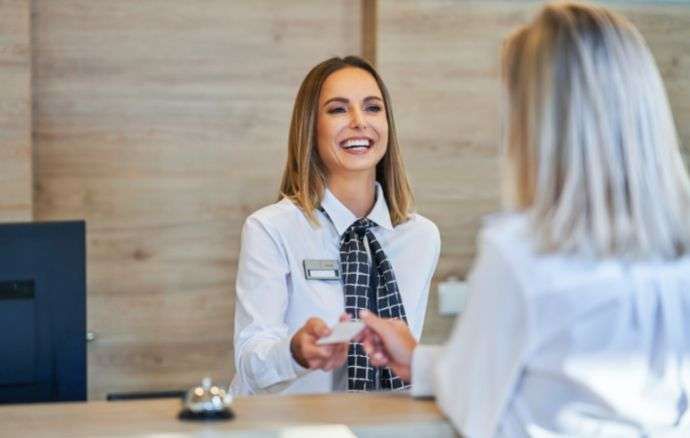 La receptionist dell'hotel sorride e porge un biglietto da visita a una donna su una scrivania di legno.