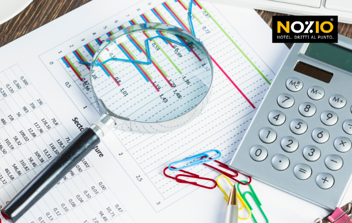 Lente d'ingrandimento su un grafico e dati finanziari, con una calcolatrice e delle graffette nelle vicinanze.