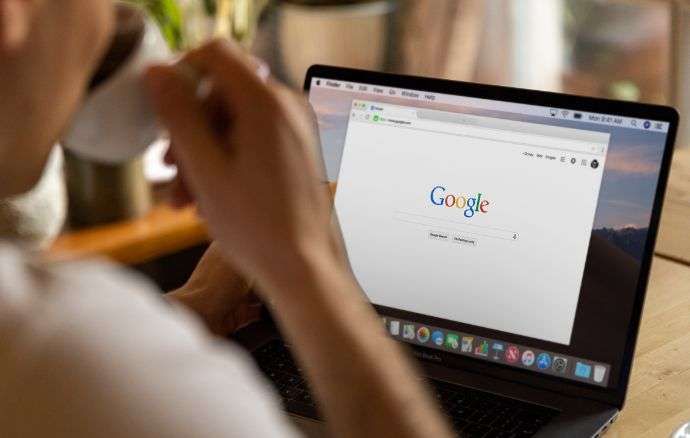 Persona che usa un computer portatile con Google aperto e beve da una tazza.