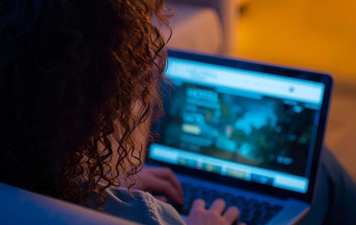 Persona con i capelli ricci, vista da dietro, che usa un laptop per cercare un hotel