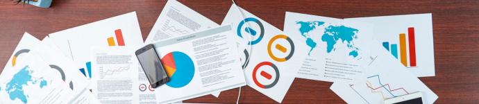 Documenti con tabelle e grafici, uno smartphone su una scrivania di legno e analisi di dati colorate.