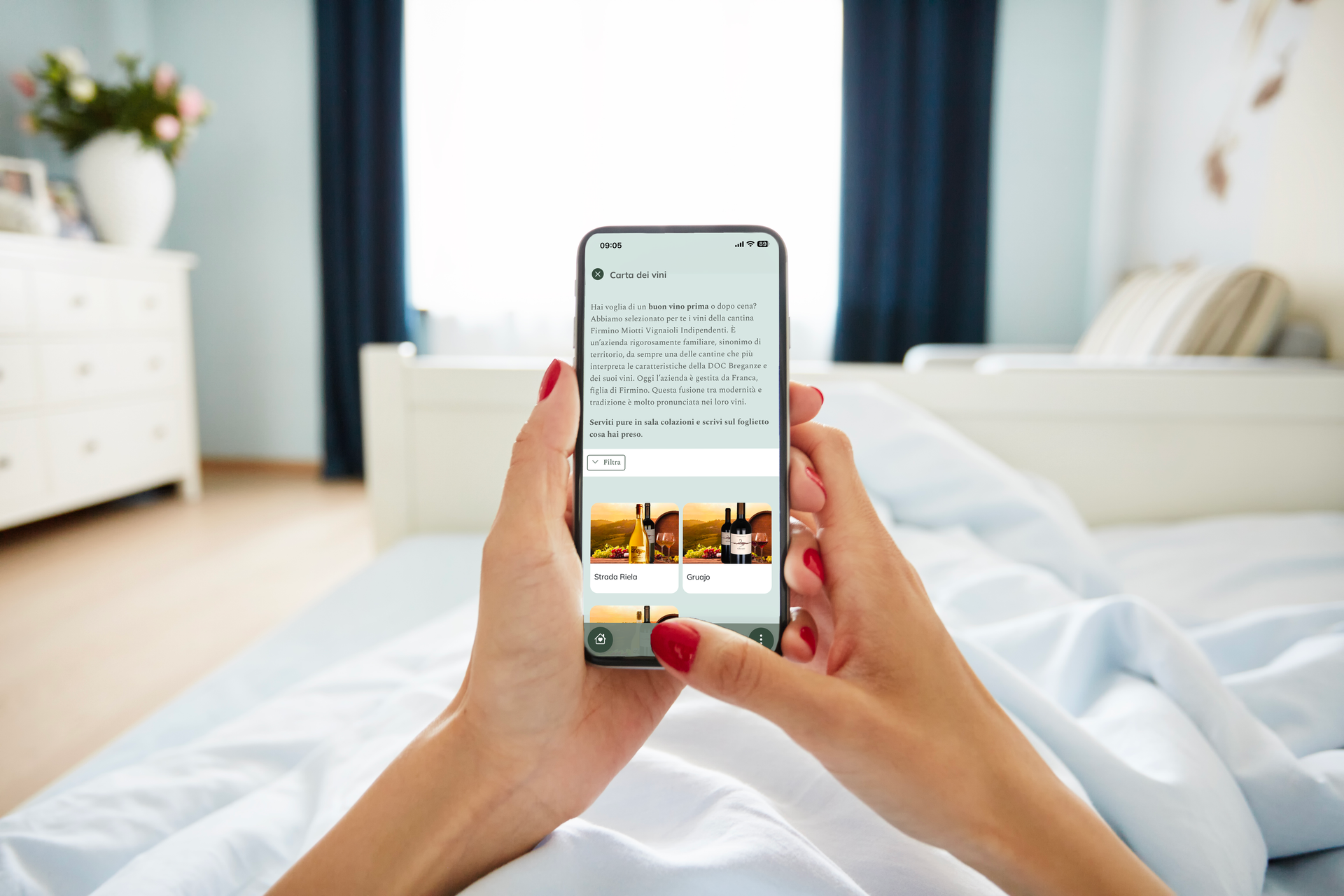 Un ospite in hotel tiene in mano uno smartphone a letto e visualizza la web app del concierge digitale che propone esperienze enogastronomiche.