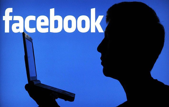 Silhouette di una persona che usa un computer portatile davanti a uno sfondo blu con il logo di Facebook.